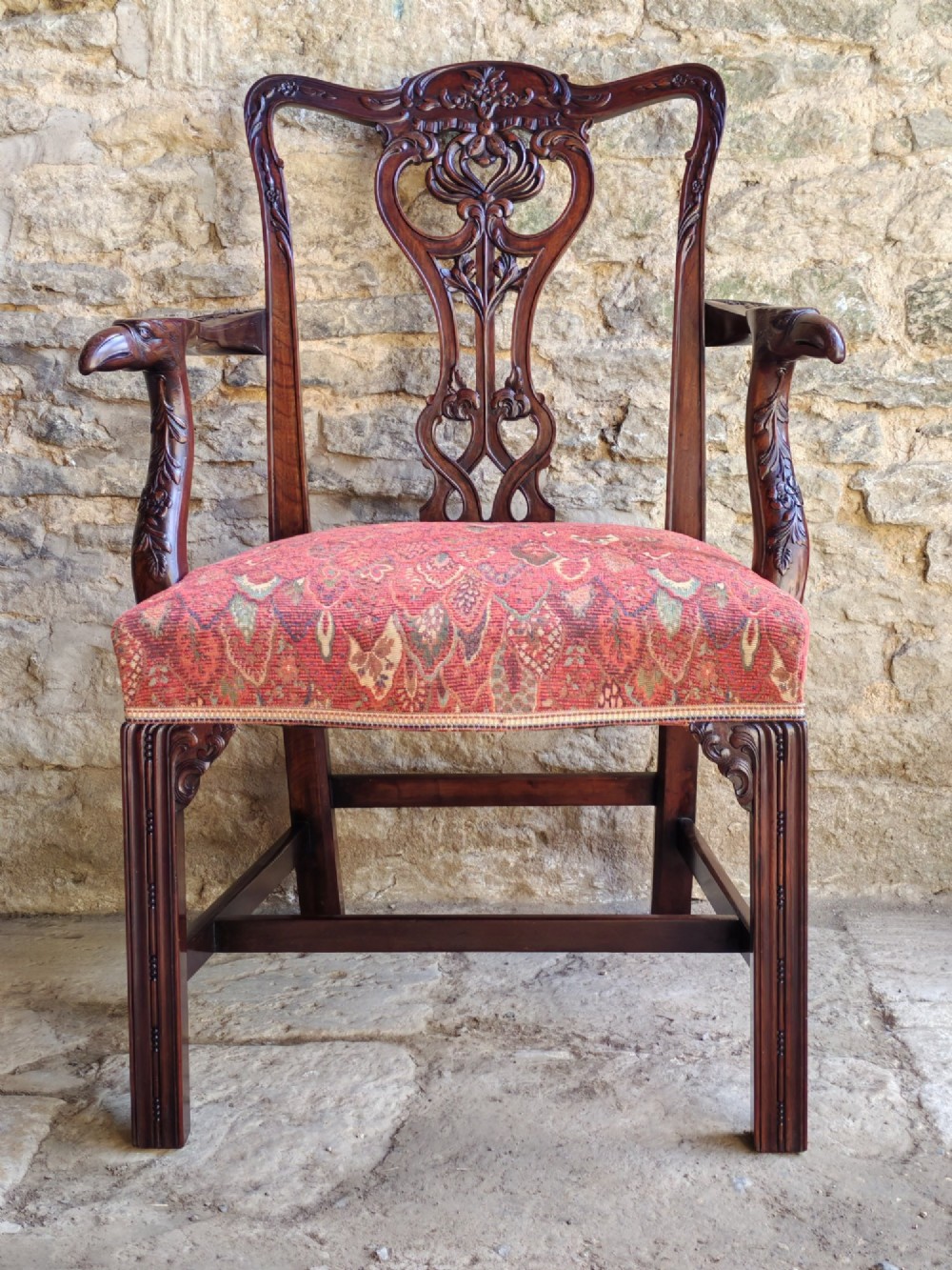 An antique dark mahogany carver armchair with a carved pierced splat back, eagle head armrests, patterned red upholstered seat, and square legs with an H-stretcher. View II