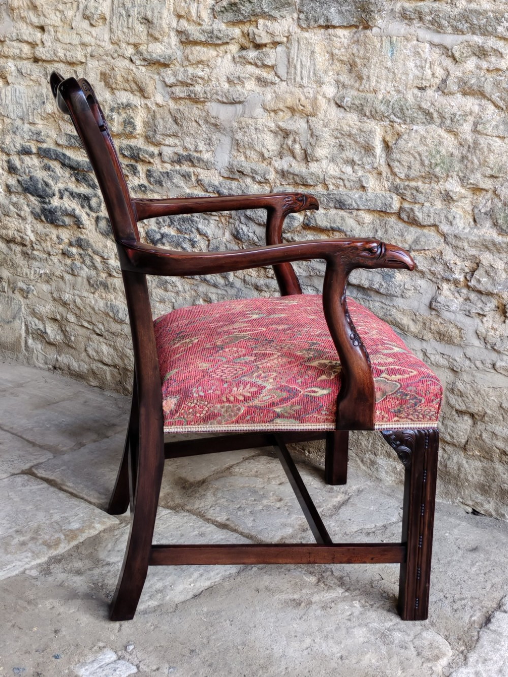 An antique dark mahogany carver armchair with a carved pierced splat back, eagle head armrests, patterned red upholstered seat, and square legs with an H-stretcher. View III