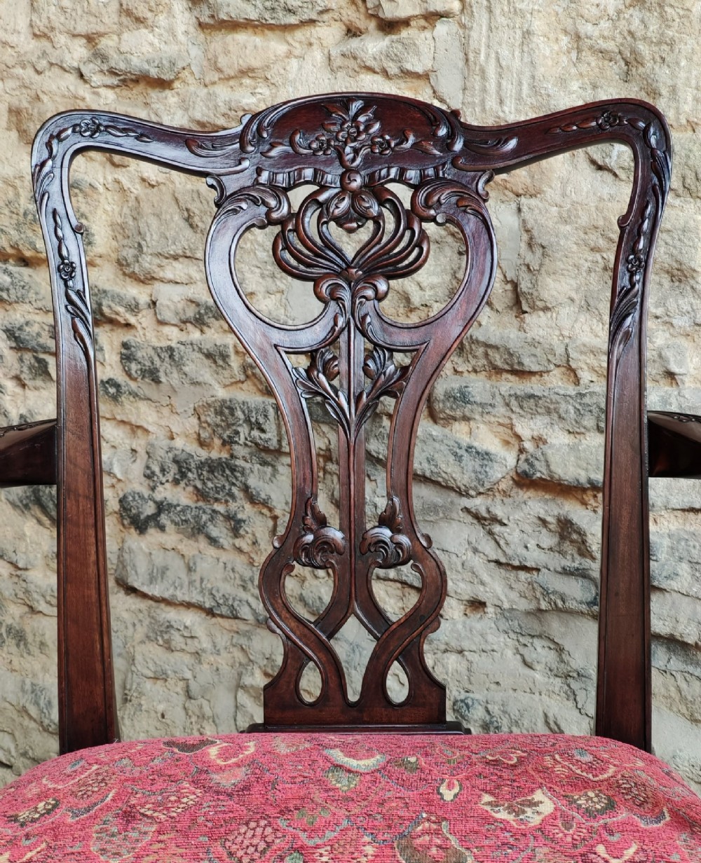 An antique dark mahogany carver armchair with a carved pierced splat back, eagle head armrests, patterned red upholstered seat, and square legs with an H-stretcher. View IV