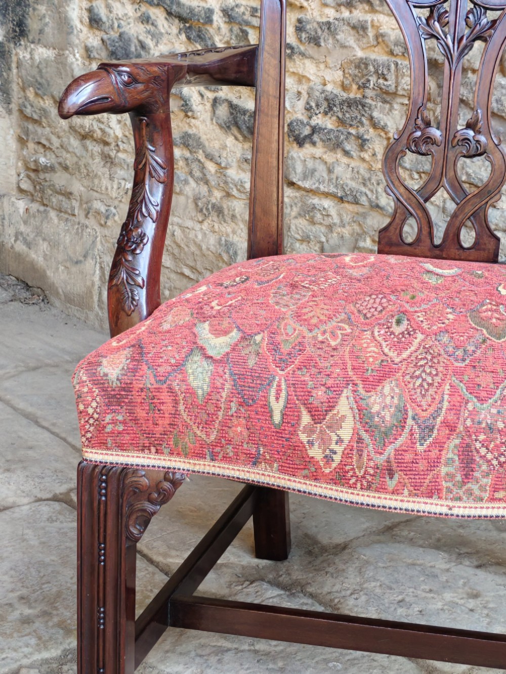 An antique dark mahogany carver armchair with a carved pierced splat back, eagle head armrests, patterned red upholstered seat, and square legs with an H-stretcher. View VI