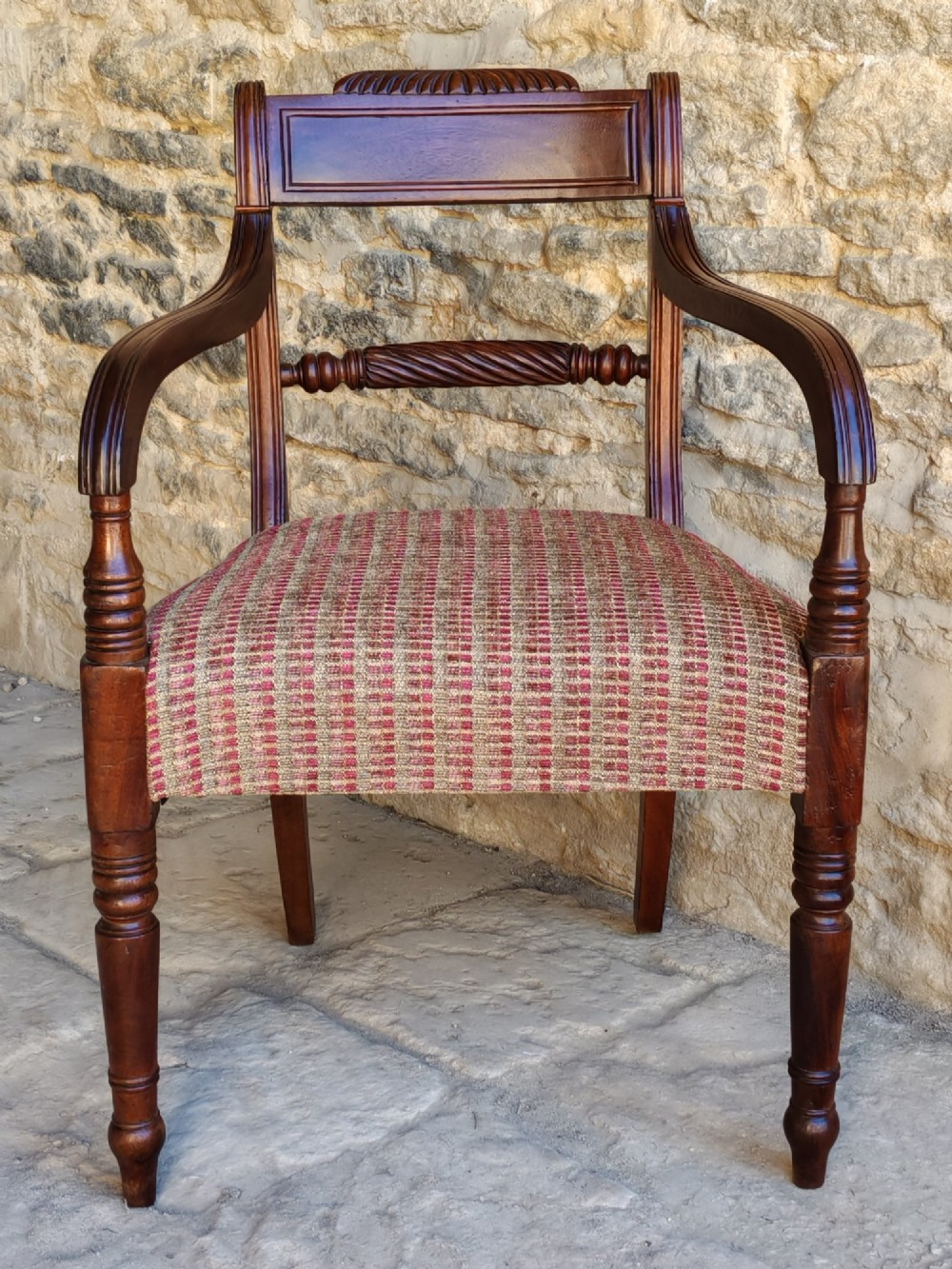 A Regency dark mahogany carver chair featuring a carved rope twist back rail, curved armrests, turned front legs, and a patterned woven upholstery seat.