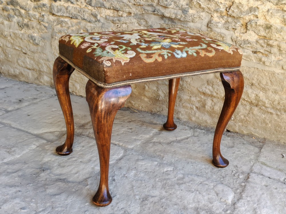 An antique walnut footstool with cabriole legs featuring a brown needlepoint upholstered seat depicting two birds amidst flowers. View V