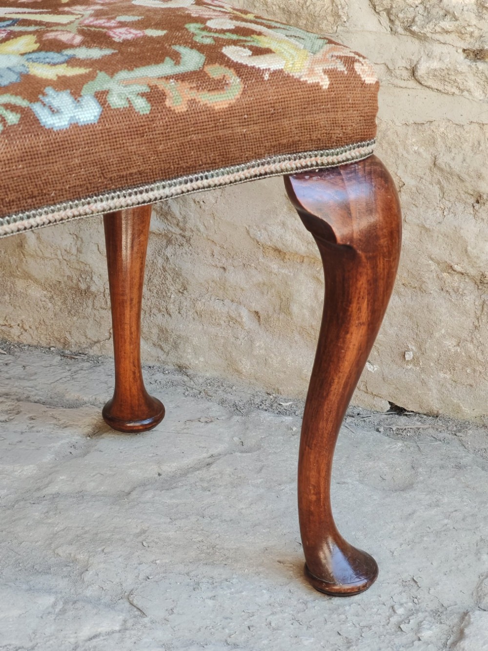 An antique walnut footstool with cabriole legs featuring a brown needlepoint upholstered seat depicting two birds amidst flowers. View VI
