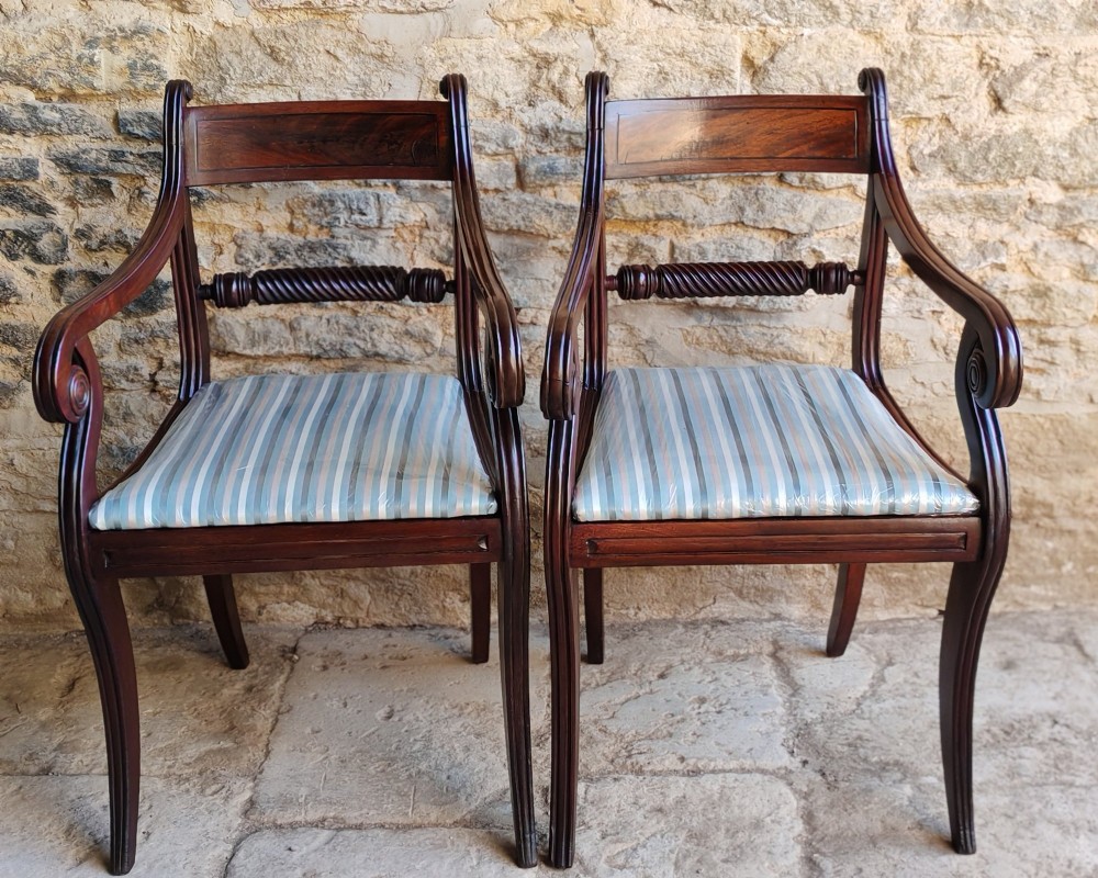 A pair of Regency mahogany carver dining chairs featuring rope-twist back rails, reeded scrolled arms, sabre front legs, and light blue striped upholstered seats.