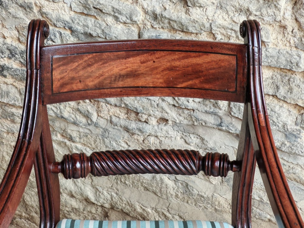 A pair of Regency mahogany carver dining chairs featuring rope-twist back rails, reeded scrolled arms, sabre front legs, and light blue striped upholstered seats. View IV