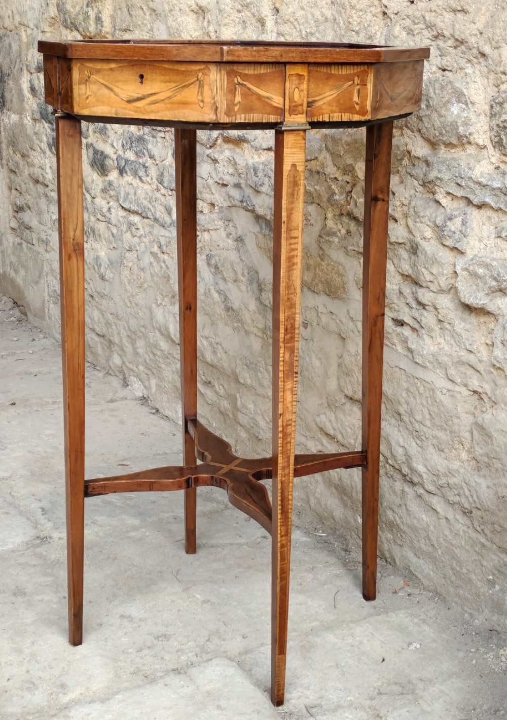 An octagonal late Victorian wood bijouterie table with marquetry swags, a glazed top displaying a pink fabric lining, tapering square legs, and a shaped cross-stretcher. View II
