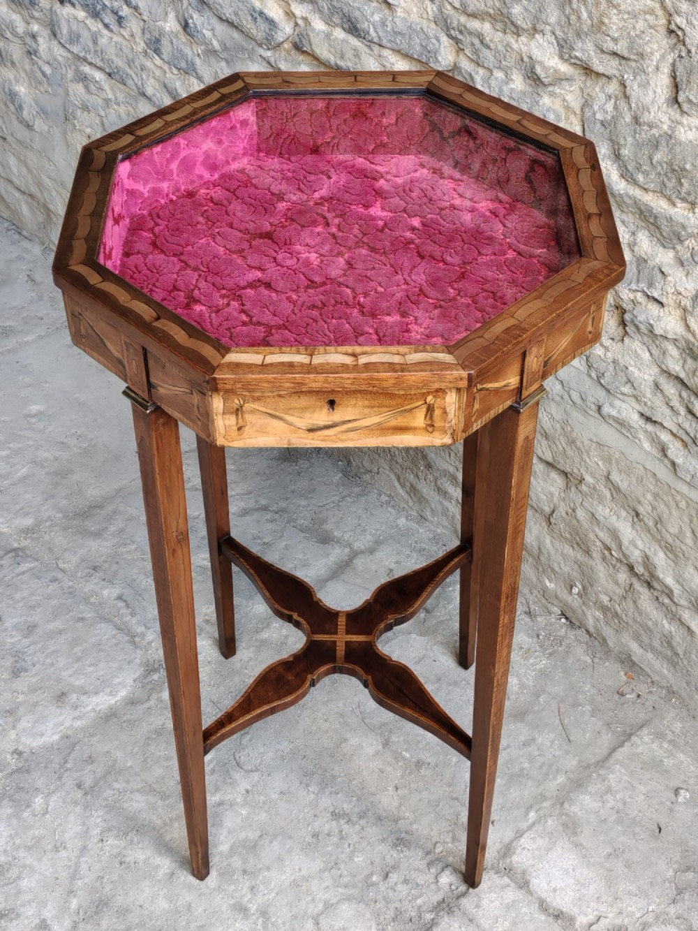 An octagonal late Victorian wood bijouterie table with marquetry swags, a glazed top displaying a pink fabric lining, tapering square legs, and a shaped cross-stretcher. View III