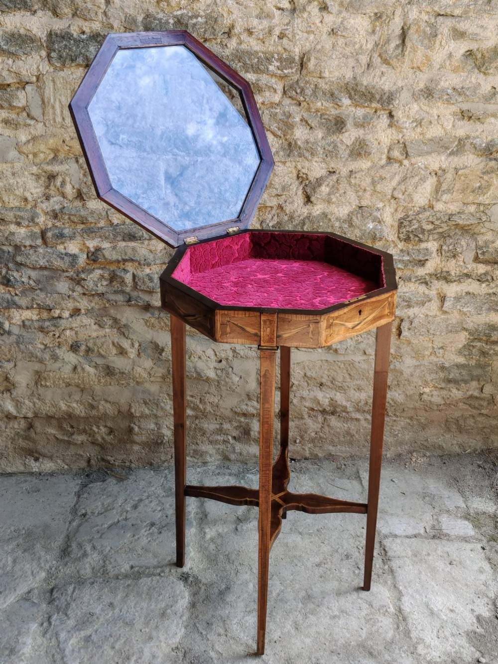 An octagonal late Victorian wood bijouterie table with marquetry swags, a glazed top displaying a pink fabric lining, tapering square legs, and a shaped cross-stretcher. View IV