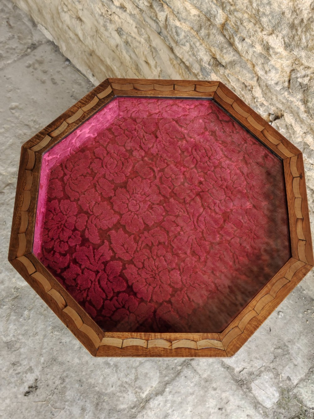 An octagonal late Victorian wood bijouterie table with marquetry swags, a glazed top displaying a pink fabric lining, tapering square legs, and a shaped cross-stretcher. View VI