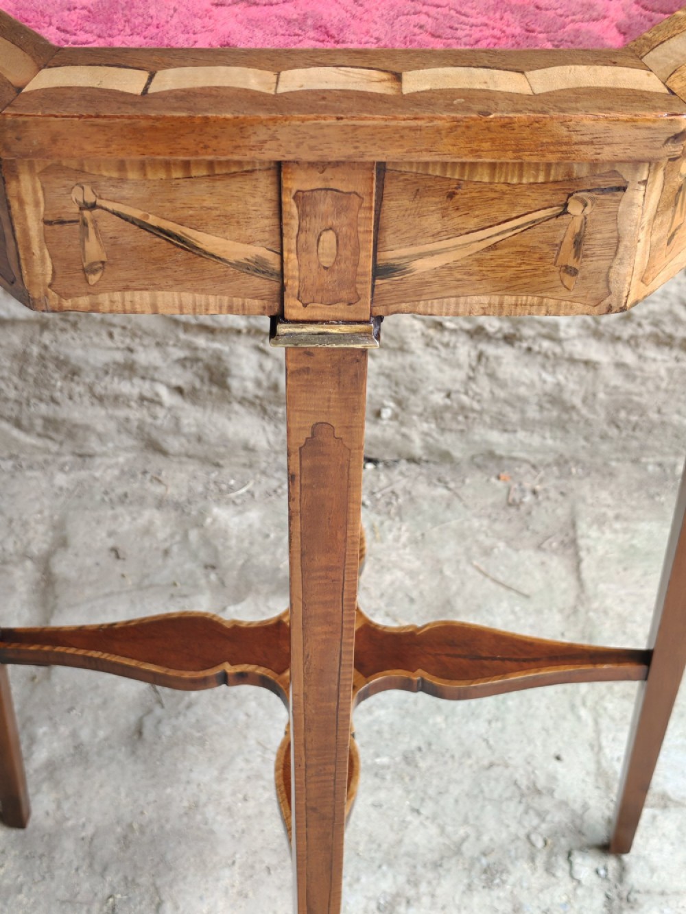 An octagonal late Victorian wood bijouterie table with marquetry swags, a glazed top displaying a pink fabric lining, tapering square legs, and a shaped cross-stretcher. View IX