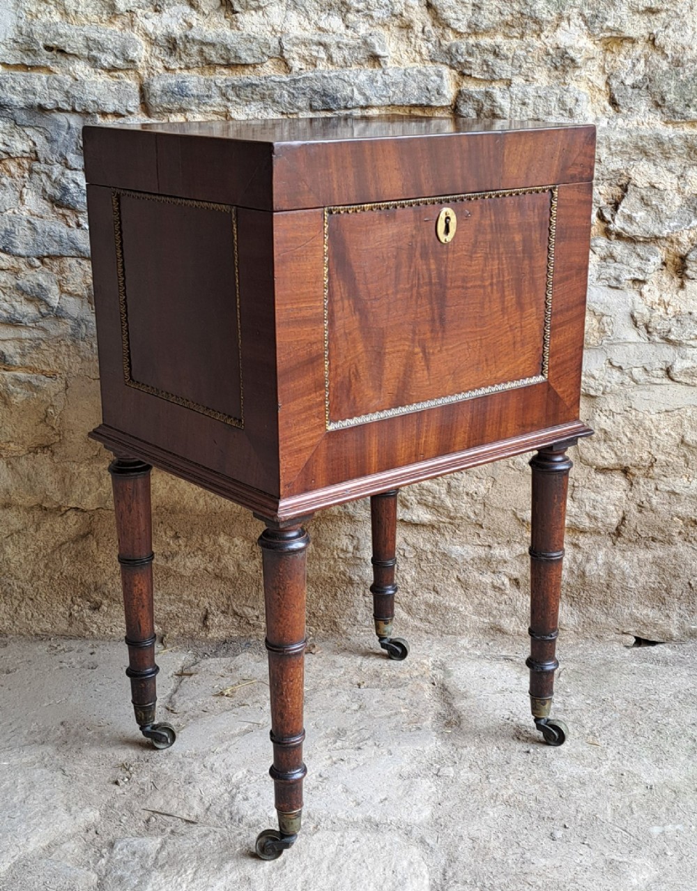 A tall Regency mahogany cellaret with a hinged lid, decorative ormolu beaded borders, a brass keyhole, and turned legs with brass castors.