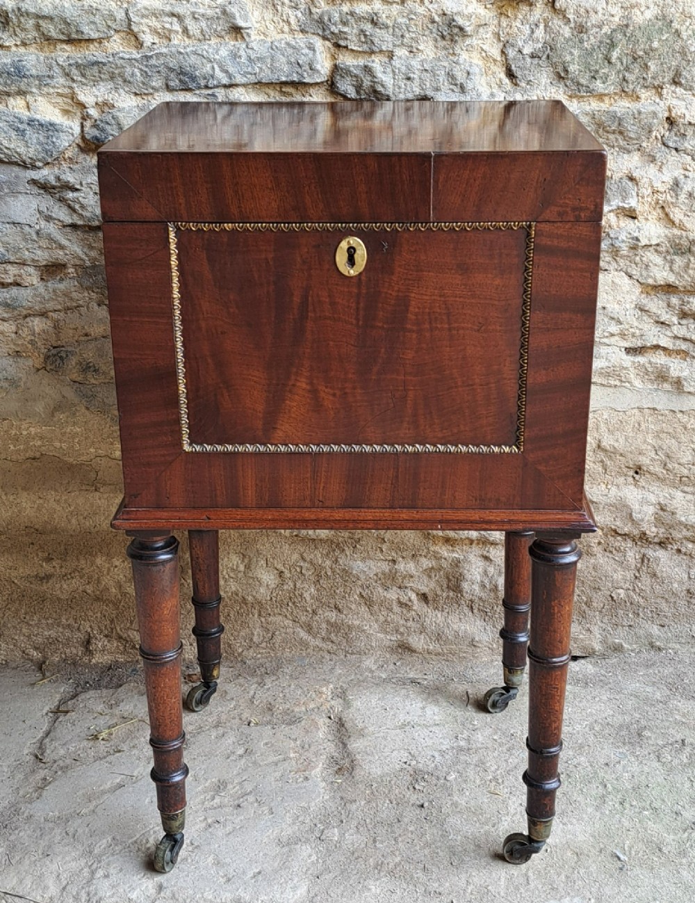 A tall Regency mahogany cellaret with a hinged lid, decorative ormolu beaded borders, a brass keyhole, and turned legs with brass castors. View II