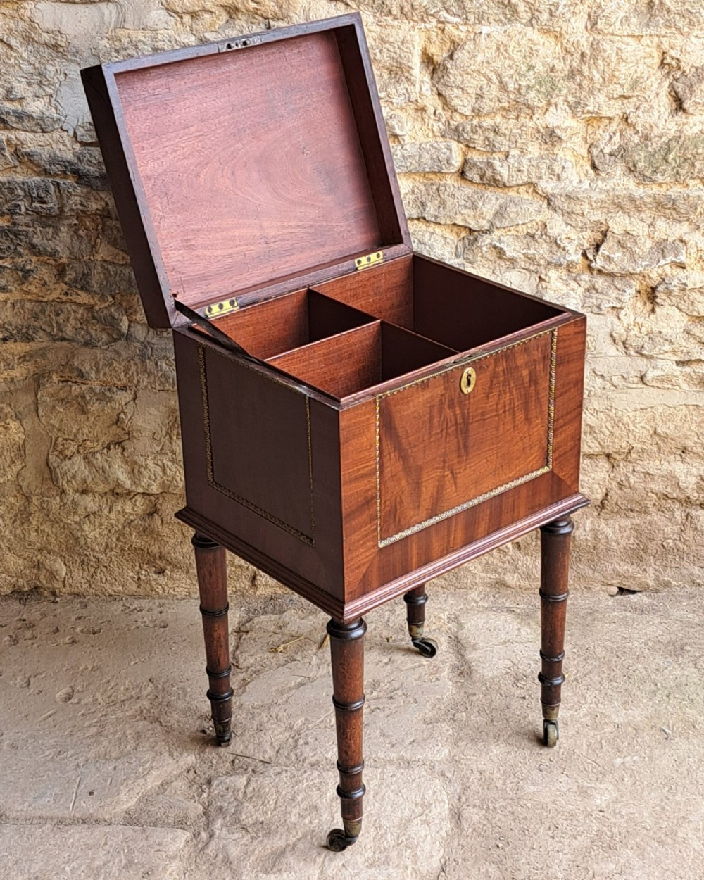 A tall Regency mahogany cellaret with a hinged lid, decorative ormolu beaded borders, a brass keyhole, and turned legs with brass castors. View VI
