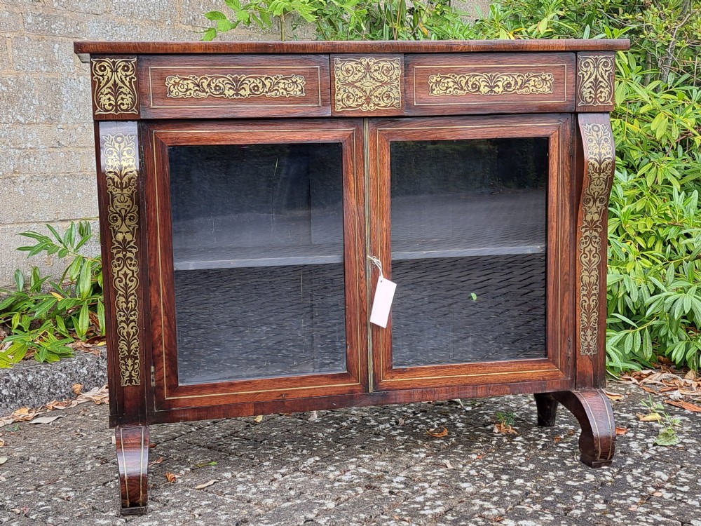 An 1830s rosewood low bookcase featuring twin glazed doors, scroll feet, and foliate brass inlay across the frieze and pilasters. View II