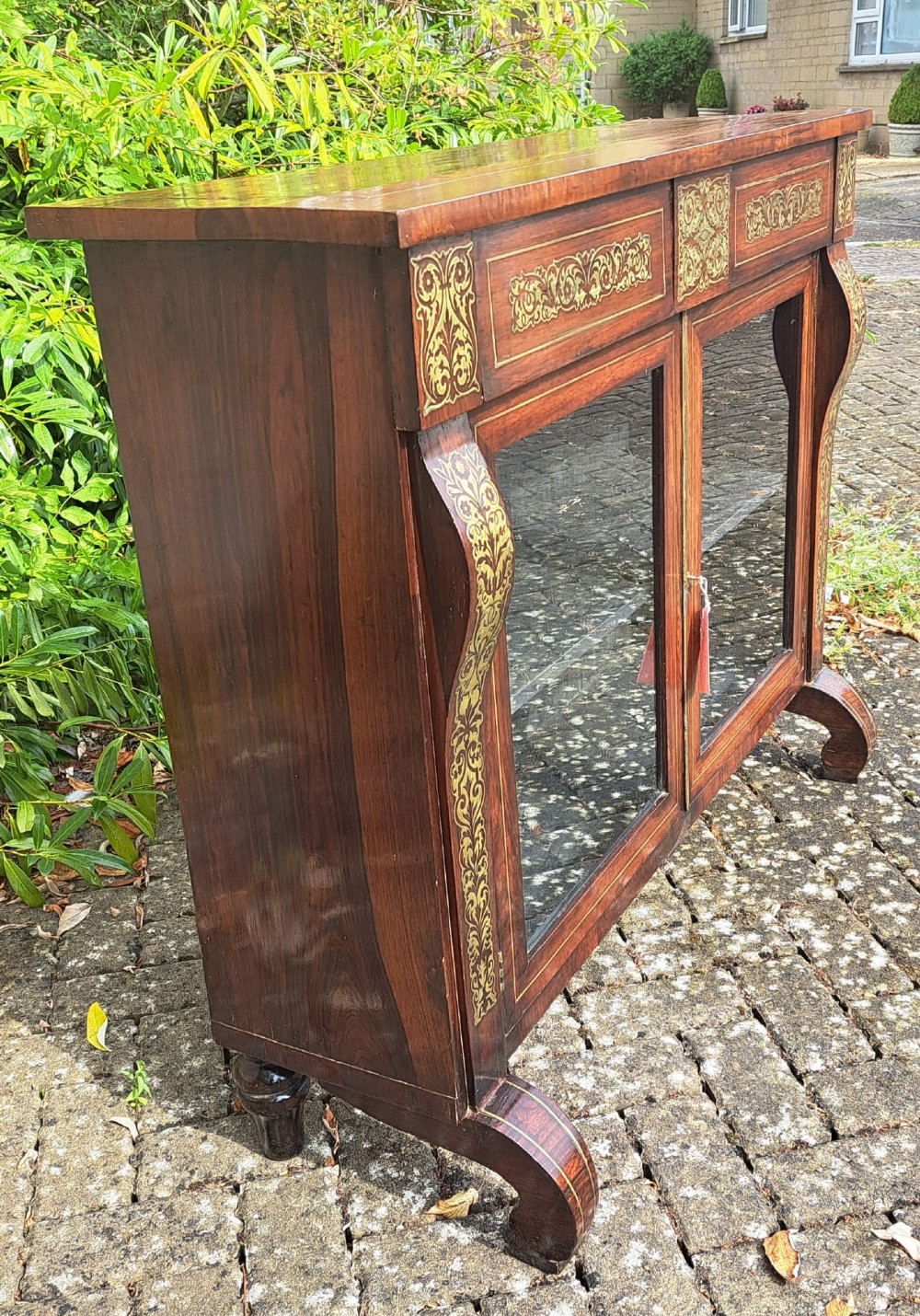 An 1830s rosewood low bookcase featuring twin glazed doors, scroll feet, and foliate brass inlay across the frieze and pilasters. View IV