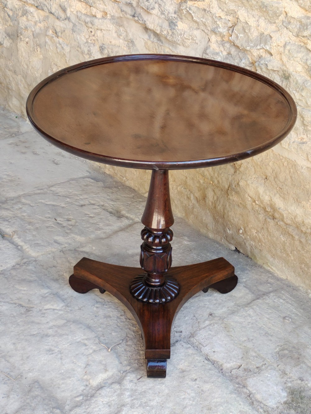 A Regency period dark mahogany and rosewood circular dish top occasional table resting on a carved pedestal stem and a triform base.