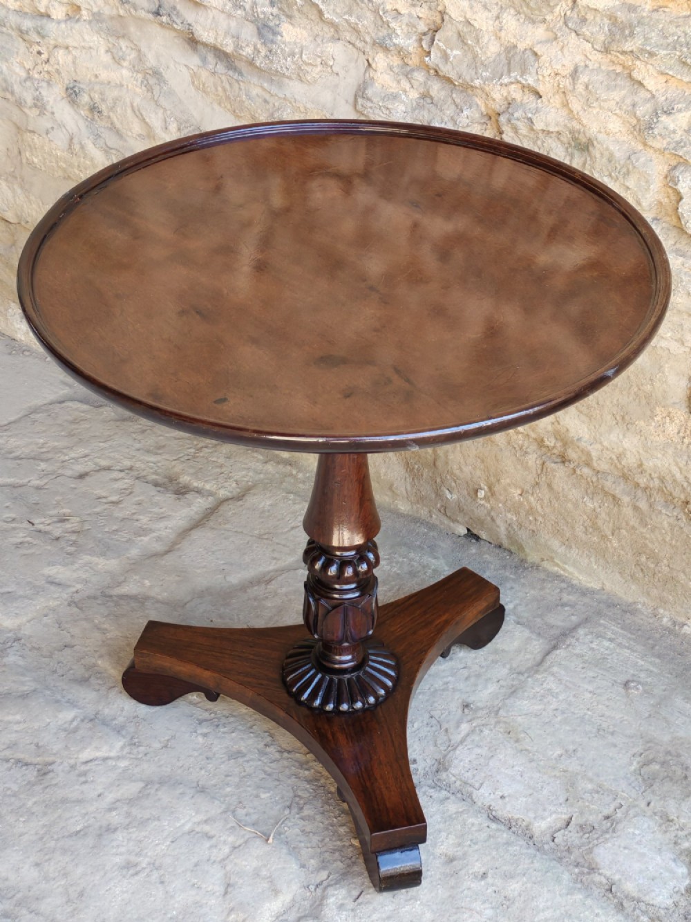 A Regency period dark mahogany and rosewood circular dish top occasional table resting on a carved pedestal stem and a triform base. View II