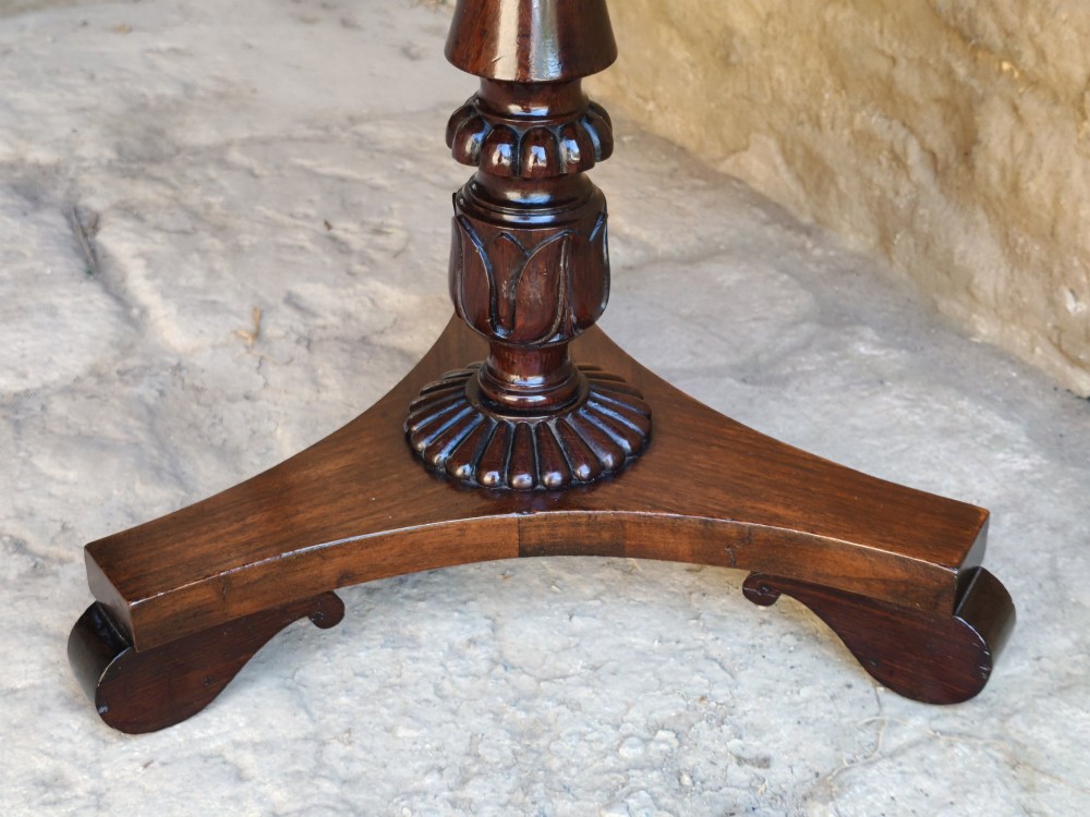 A Regency period dark mahogany and rosewood circular dish top occasional table resting on a carved pedestal stem and a triform base. View V