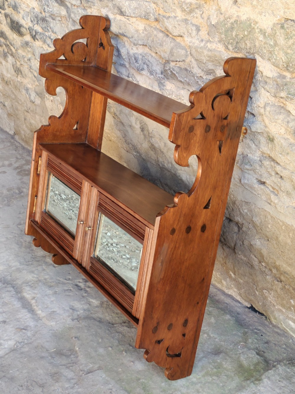 A late 19th-century warm brown walnut wall cabinet featuring pierced fretwork side panels, an upper display shelf, and twin mirrored doors at the base.