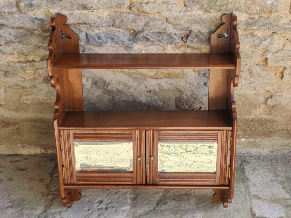 A late 19th-century warm brown walnut wall cabinet featuring pierced fretwork side panels, an upper display shelf, and twin mirrored doors at the base. View II