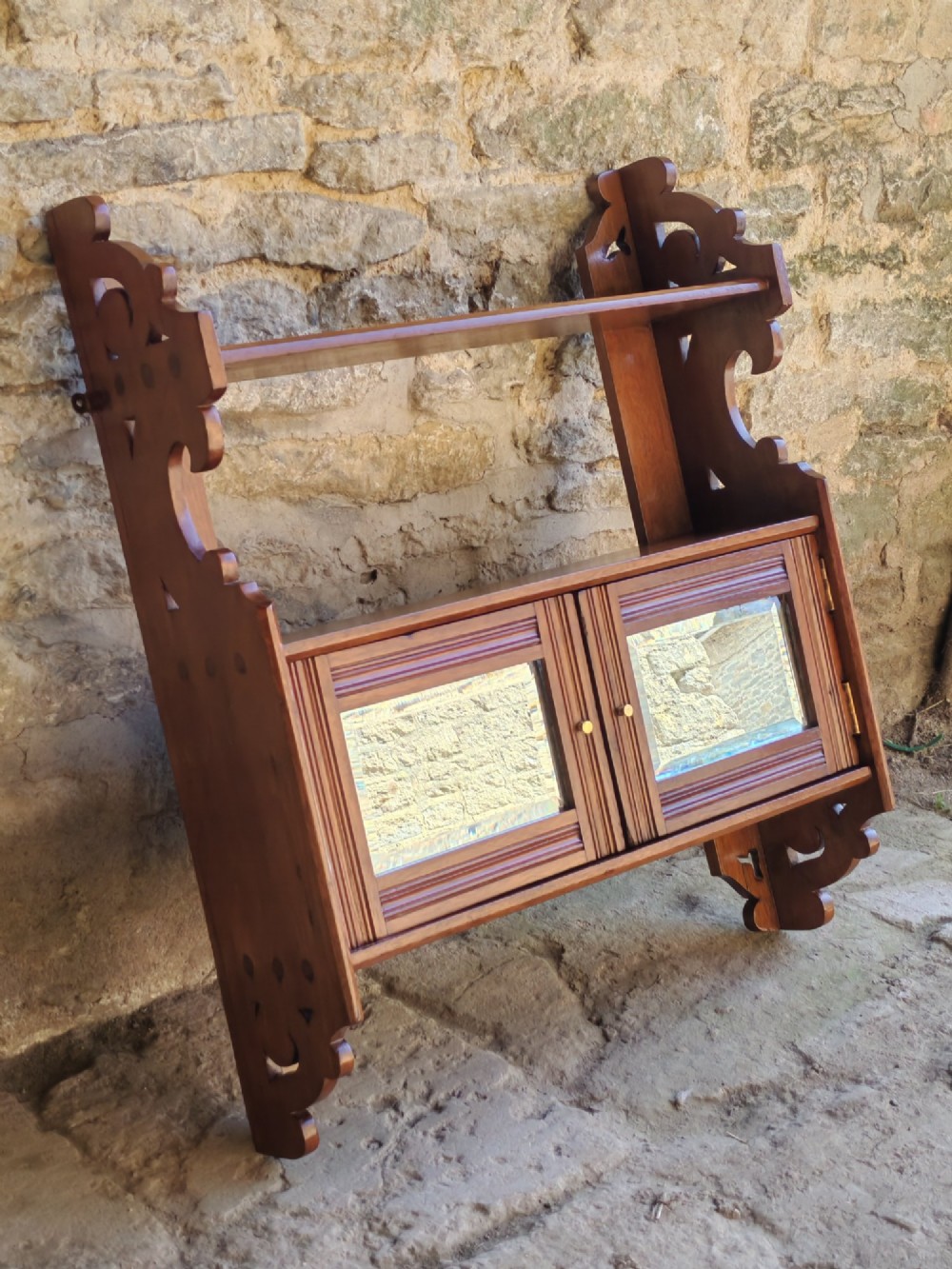 A late 19th-century warm brown walnut wall cabinet featuring pierced fretwork side panels, an upper display shelf, and twin mirrored doors at the base. View III