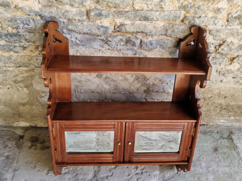 A late 19th-century warm brown walnut wall cabinet featuring pierced fretwork side panels, an upper display shelf, and twin mirrored doors at the base. View IV