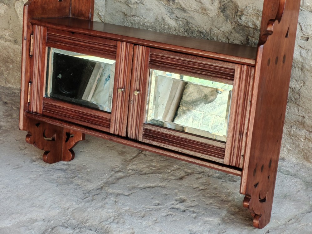 A late 19th-century warm brown walnut wall cabinet featuring pierced fretwork side panels, an upper display shelf, and twin mirrored doors at the base. View V