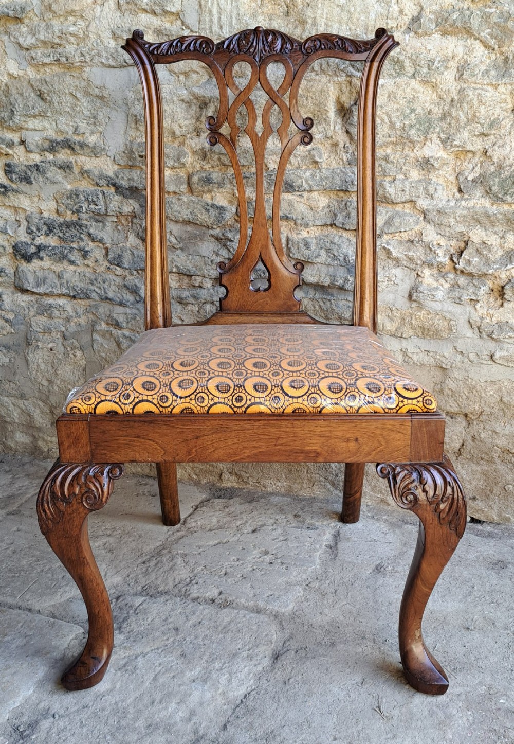 A 19th-century walnut side chair featuring an intricately carved pierced back splat, cabriole legs with carved knees, and a patterned upholstered seat.