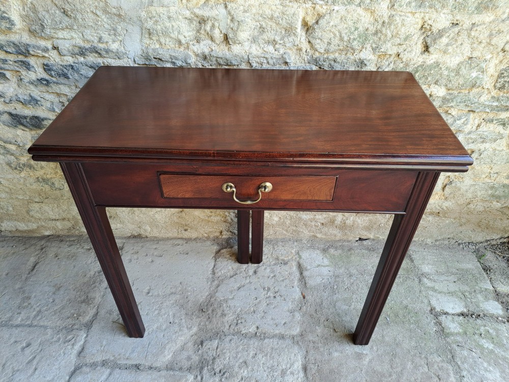 An 18th-century Georgian Cuban mahogany tea table featuring a rectangular foldover top, a single drawer with a brass handle, and straight moulded legs.