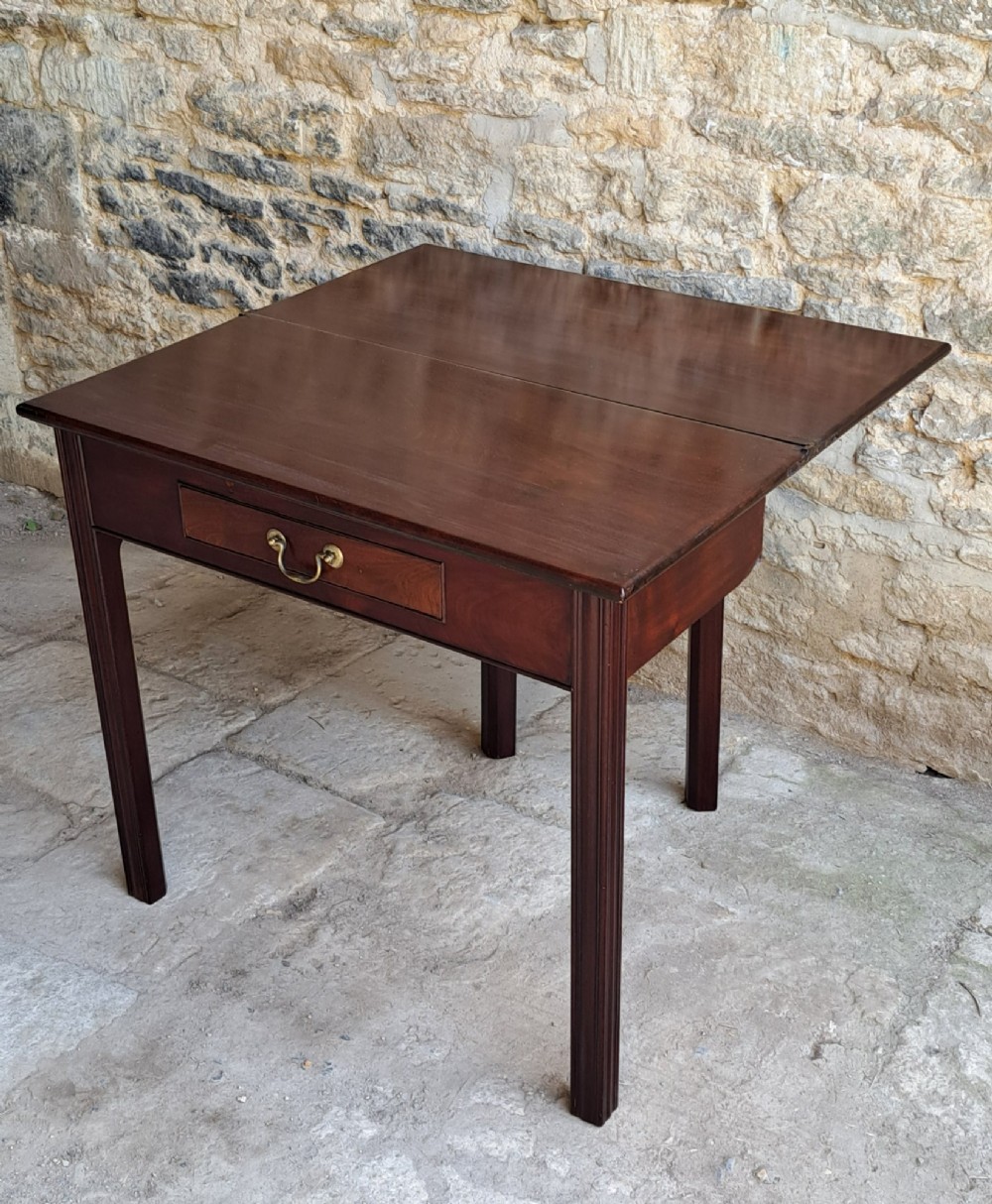 An 18th-century Georgian Cuban mahogany tea table featuring a rectangular foldover top, a single drawer with a brass handle, and straight moulded legs. View V