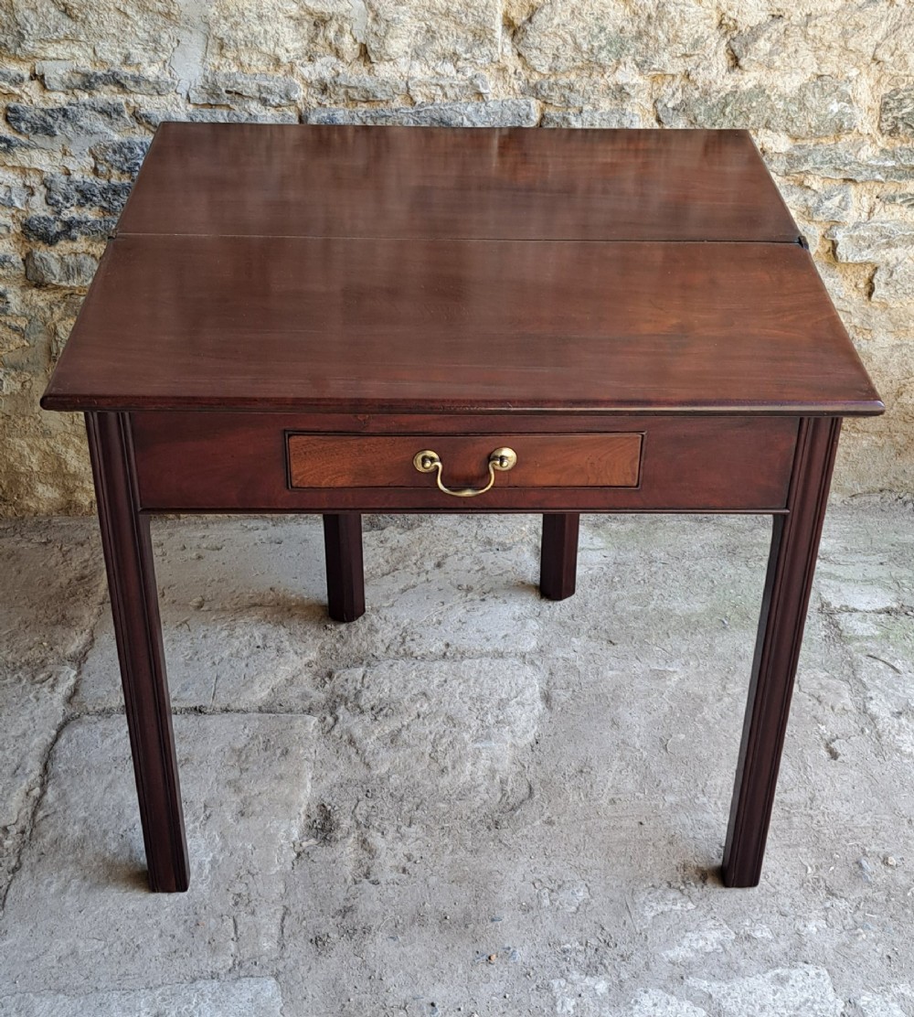 An 18th-century Georgian Cuban mahogany tea table featuring a rectangular foldover top, a single drawer with a brass handle, and straight moulded legs. View VI