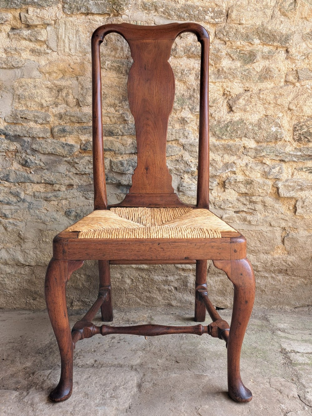 A Queen Anne walnut side chair featuring a solid vase-shaped back splat, a woven rush seat, cabriole front legs with pad feet, and turned stretchers.