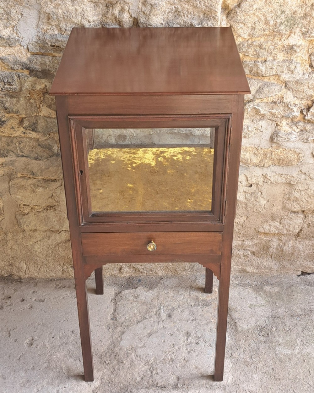 A Georgian mahogany standing display cabinet featuring a glass-enclosed upper section lined with gold fabric, a single lower drawer, and square tapered legs. View III