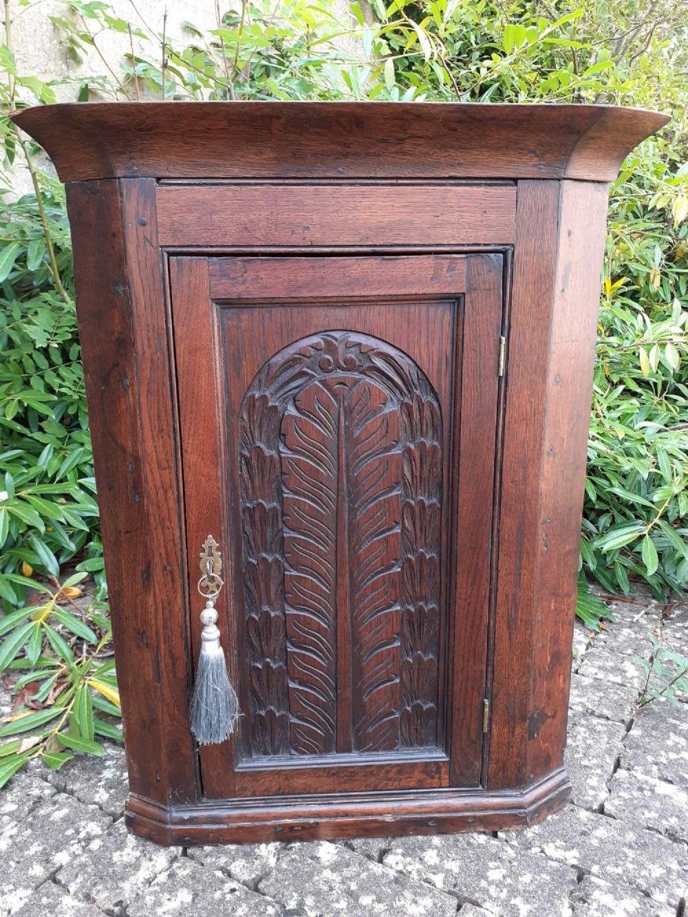 An 18th-century dark oak hanging corner cupboard featuring a single hand-carved foliate panel door and brass escutcheon.
