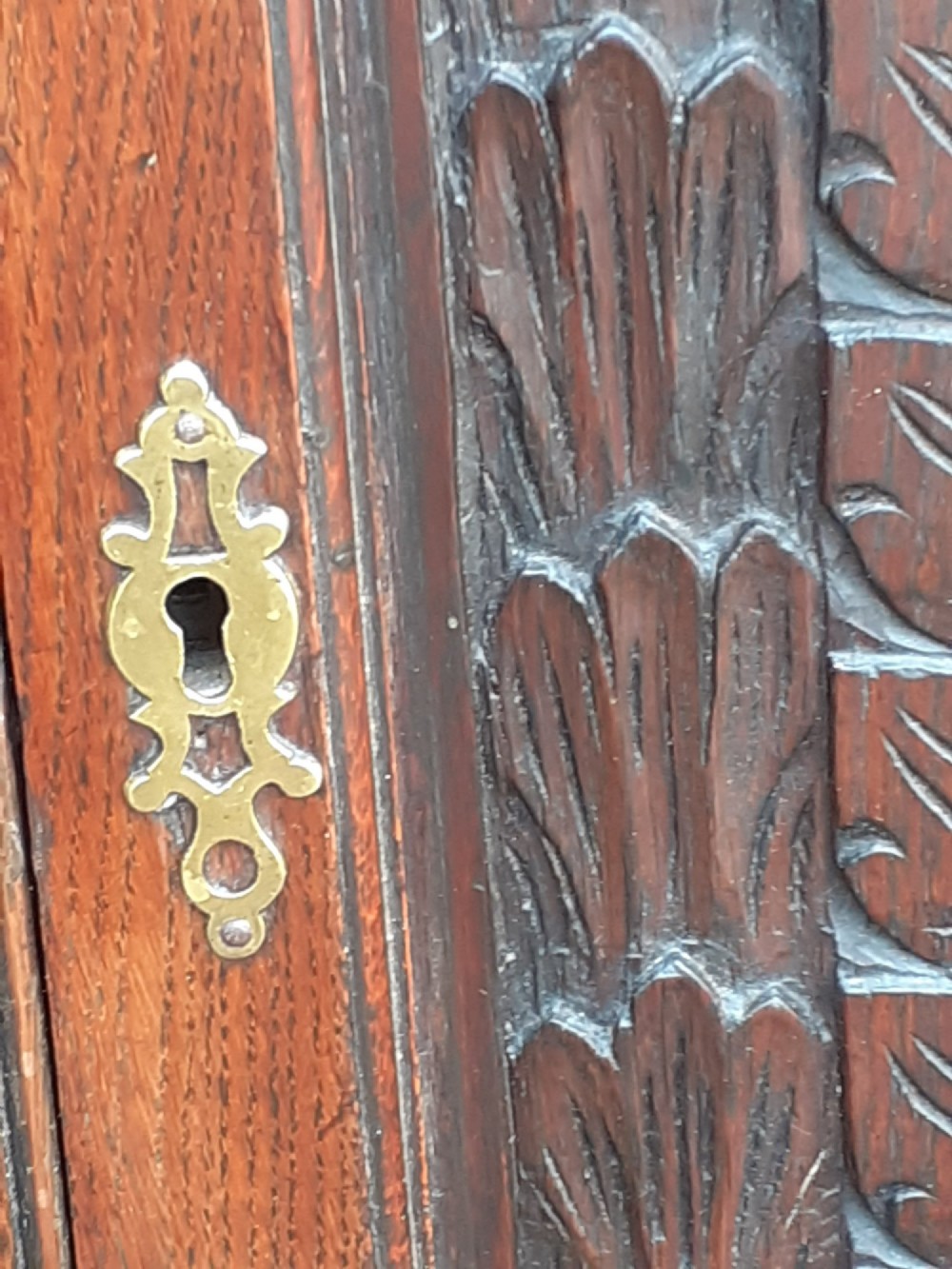 An 18th-century dark oak hanging corner cupboard featuring a single hand-carved foliate panel door and brass escutcheon. View IV