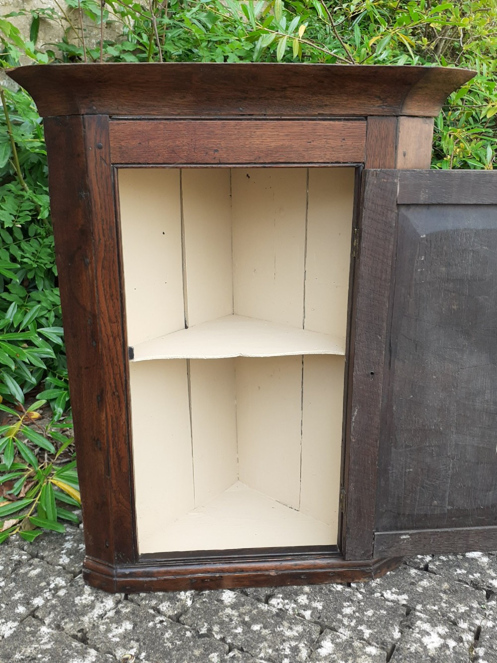 An 18th-century dark oak hanging corner cupboard featuring a single hand-carved foliate panel door and brass escutcheon. View V