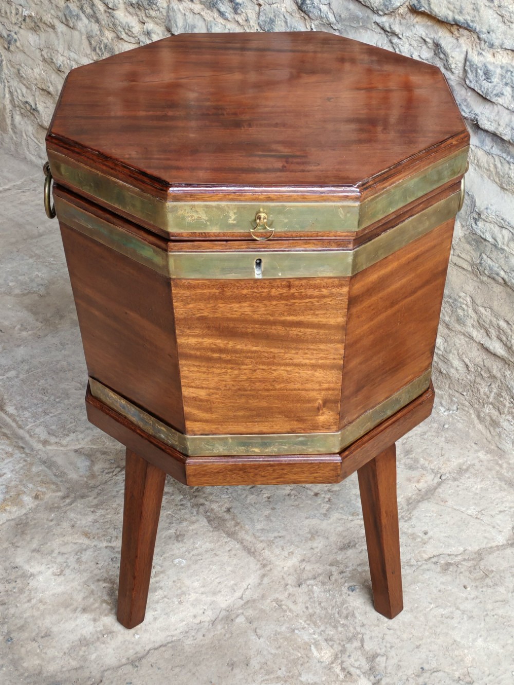 An 18th-century octagonal mahogany wine cooler with brass bindings, brass handles, and four tapered square legs.