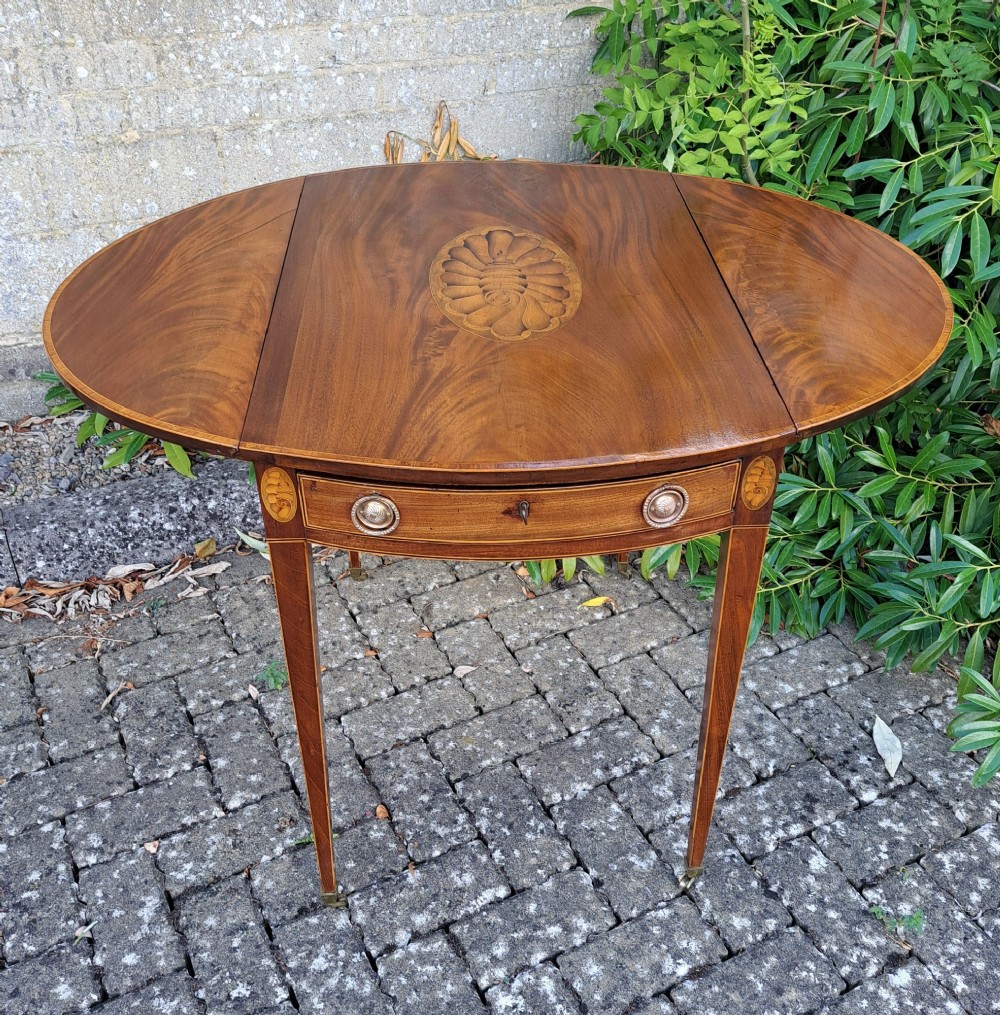 A George III mahogany drop-leaf Pembroke table featuring an oval satinwood shell inlay medallion, drawer with brass ring handles, and square tapered legs on brass castors.