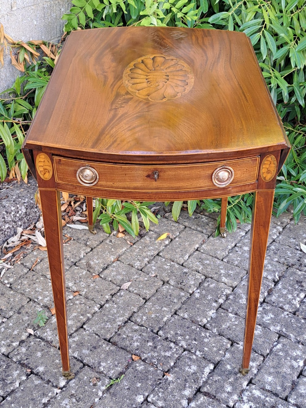 A George III mahogany drop-leaf Pembroke table featuring an oval satinwood shell inlay medallion, drawer with brass ring handles, and square tapered legs on brass castors. View II