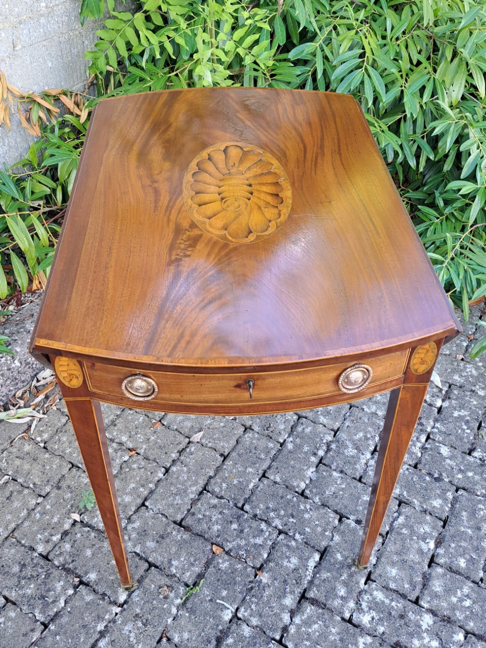 A George III mahogany drop-leaf Pembroke table featuring an oval satinwood shell inlay medallion, drawer with brass ring handles, and square tapered legs on brass castors. View III