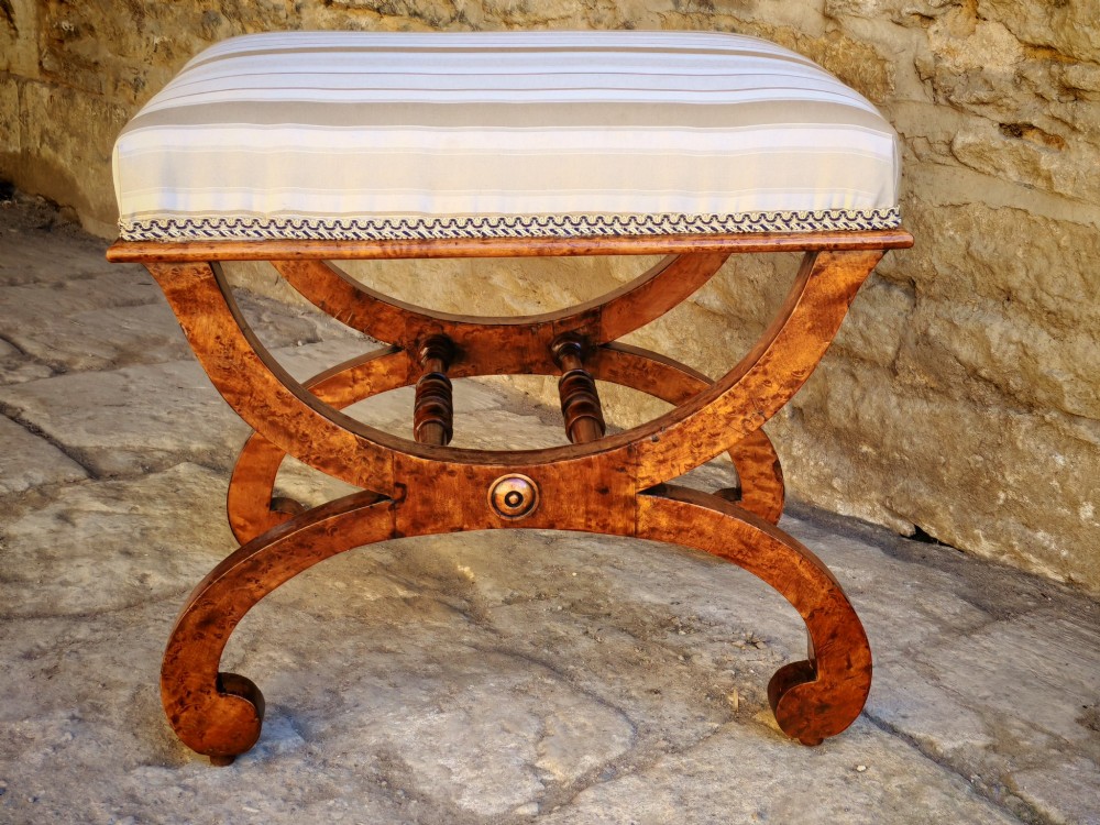 A mid-19th century X-frame stool crafted from figured burr maple, featuring a central turned stretcher and a neutral striped fabric upholstered seat. View II