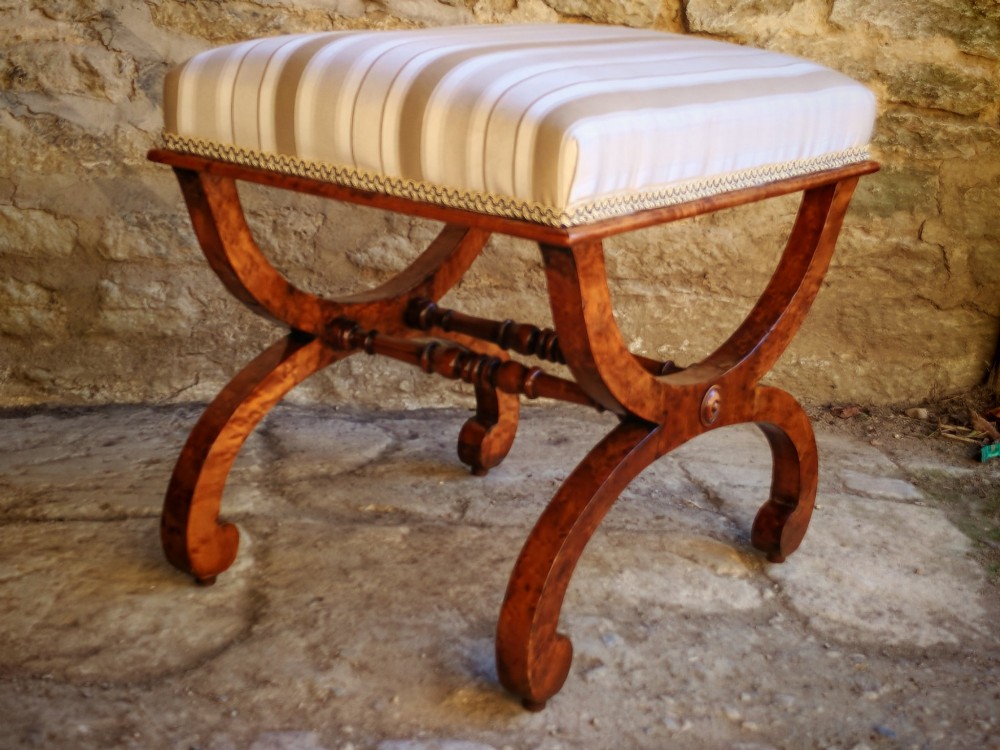 A mid-19th century X-frame stool crafted from figured burr maple, featuring a central turned stretcher and a neutral striped fabric upholstered seat. View VI