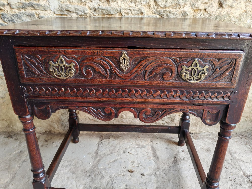 An 18th-century dark oak lowboy table featuring a hand-carved drawer front, decorative brass handles, turned legs, and a lower stretcher base. View III