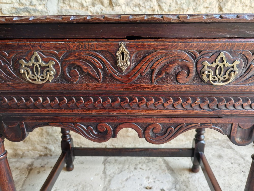 An 18th-century dark oak lowboy table featuring a hand-carved drawer front, decorative brass handles, turned legs, and a lower stretcher base. View IV