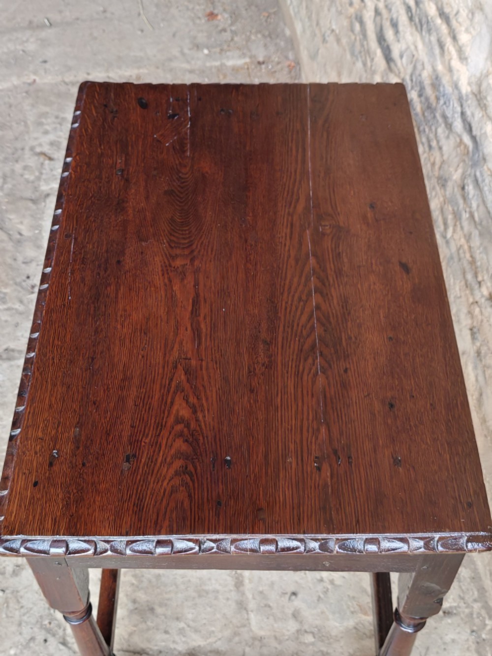 An 18th-century dark oak lowboy table featuring a hand-carved drawer front, decorative brass handles, turned legs, and a lower stretcher base. View V