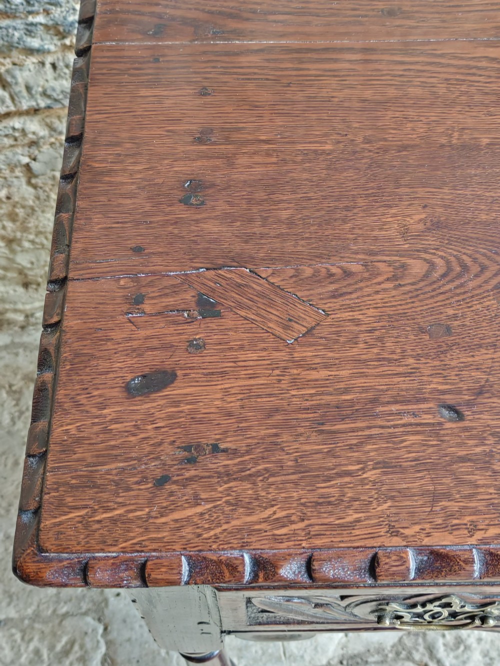 An 18th-century dark oak lowboy table featuring a hand-carved drawer front, decorative brass handles, turned legs, and a lower stretcher base. View VIII
