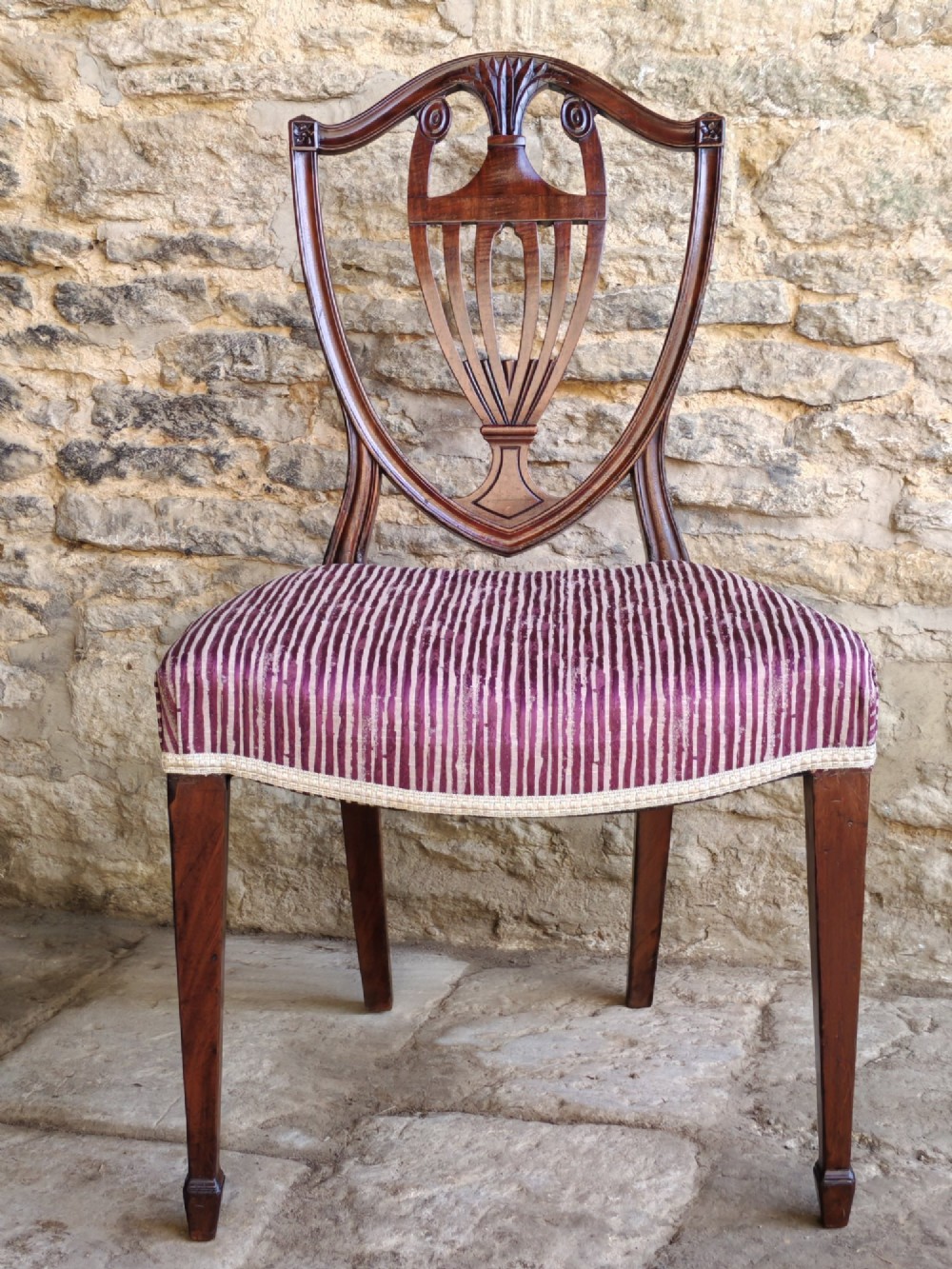 A set of six mahogany Hepplewhite dining chairs featuring carved shield backs with urn motifs and striped fabric upholstery. View II