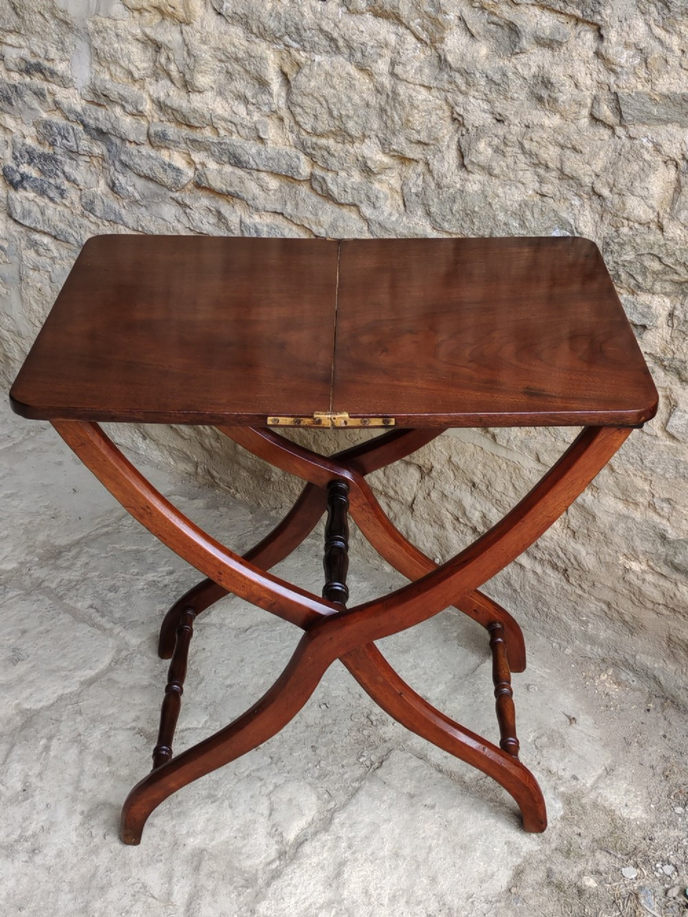 An Edwardian mahogany coaching table featuring a hinged folding rectangular top supported by curved X-frame legs and turned stretchers.