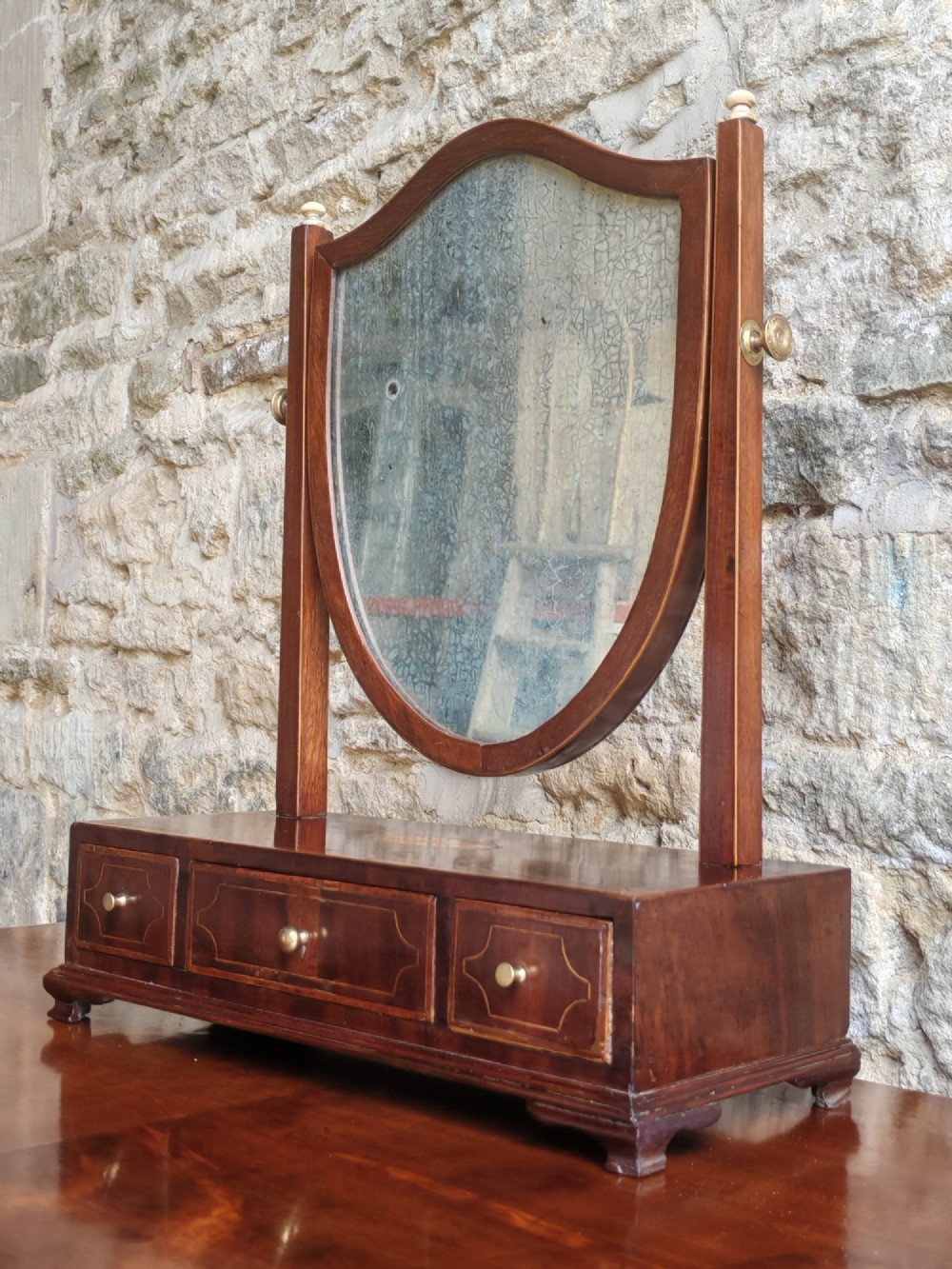 A Georgian mahogany dressing mirror featuring a shield-shaped swivel frame, bone finials, and an inlaid three-drawer box base. View II