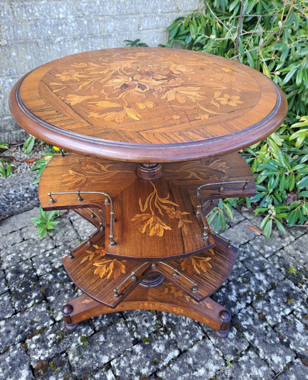 A circular Dutch marquetry revolving library table with floral wood inlays, tiered shelves featuring brass galleries, and a quadform pedestal base.
